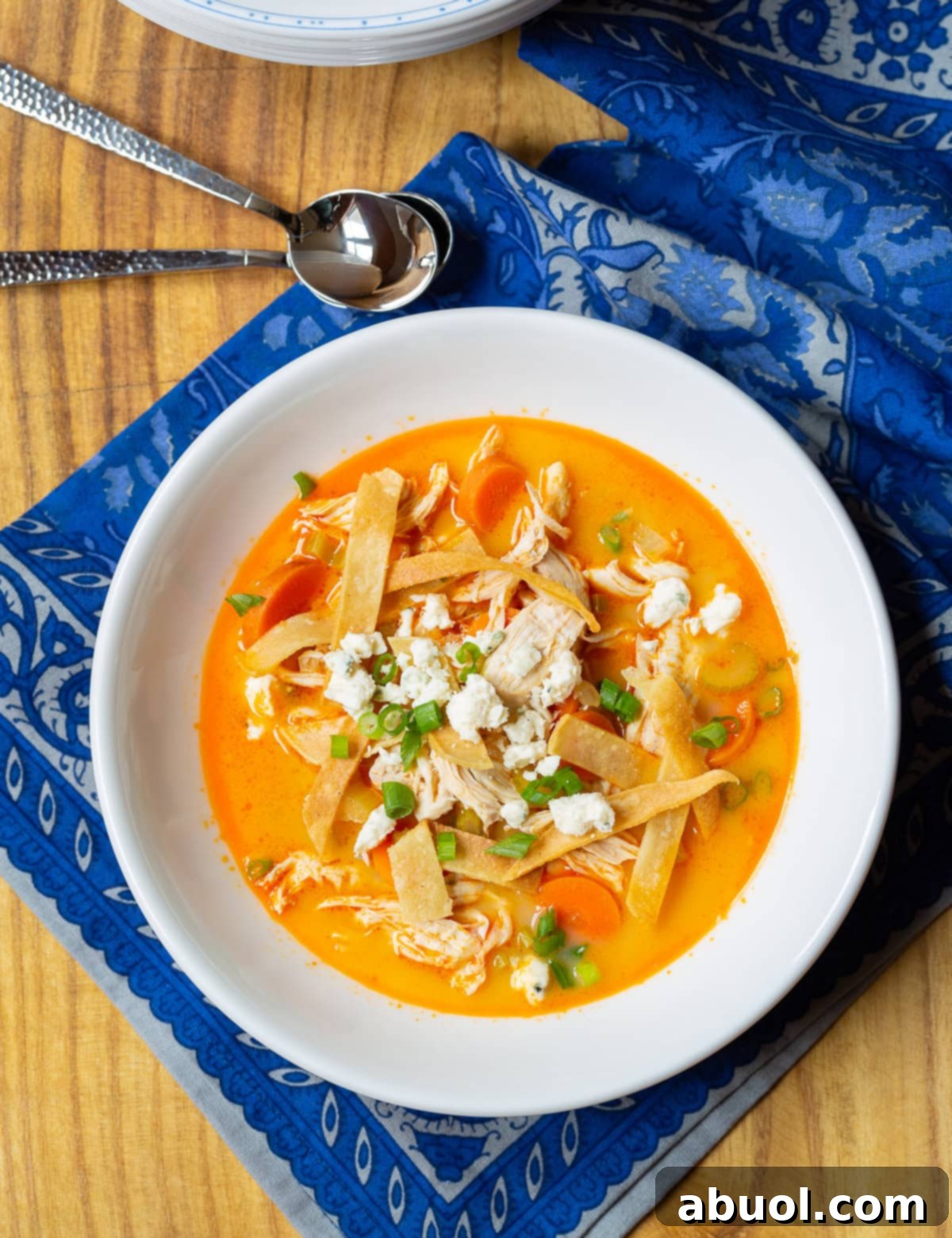 A steaming bowl of Slow Cooker Buffalo Chicken Soup in a white bowl, resting on a blue cloth, garnished with fresh herbs.