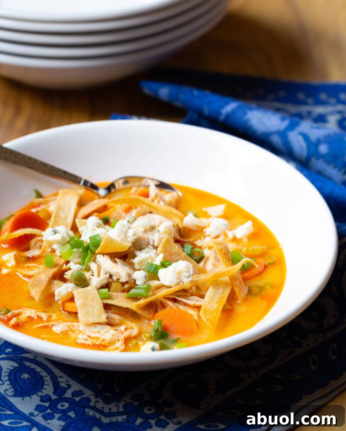 A close-up of a bowl of easy buffalo chicken soup, topped with crispy tortilla strips and fresh green onions.