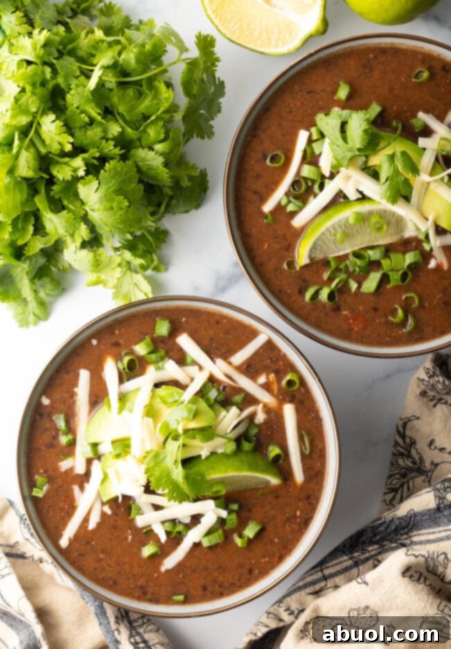 overhead shot of black bean soup in a crock pot, garnished with cheese, lime wedges, and fresh cilantro