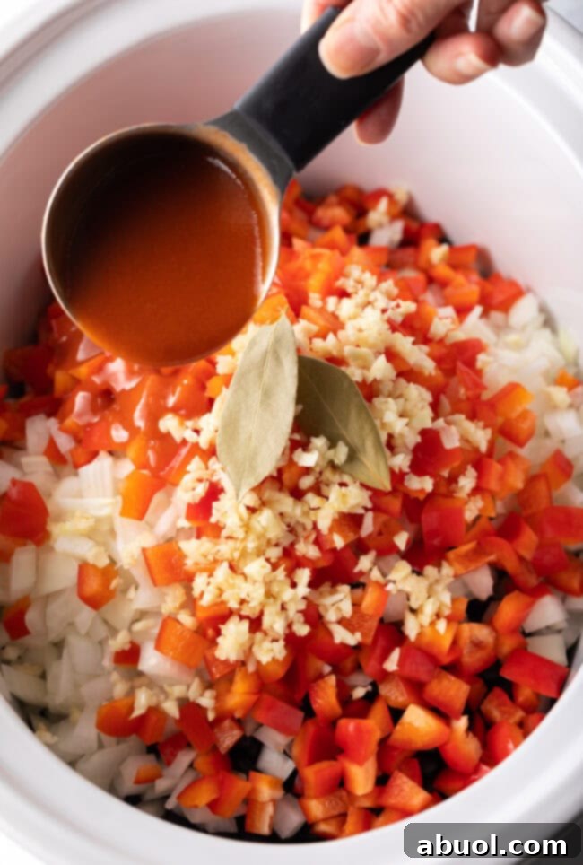 all black bean soup ingredients being added to a slow cooker pot