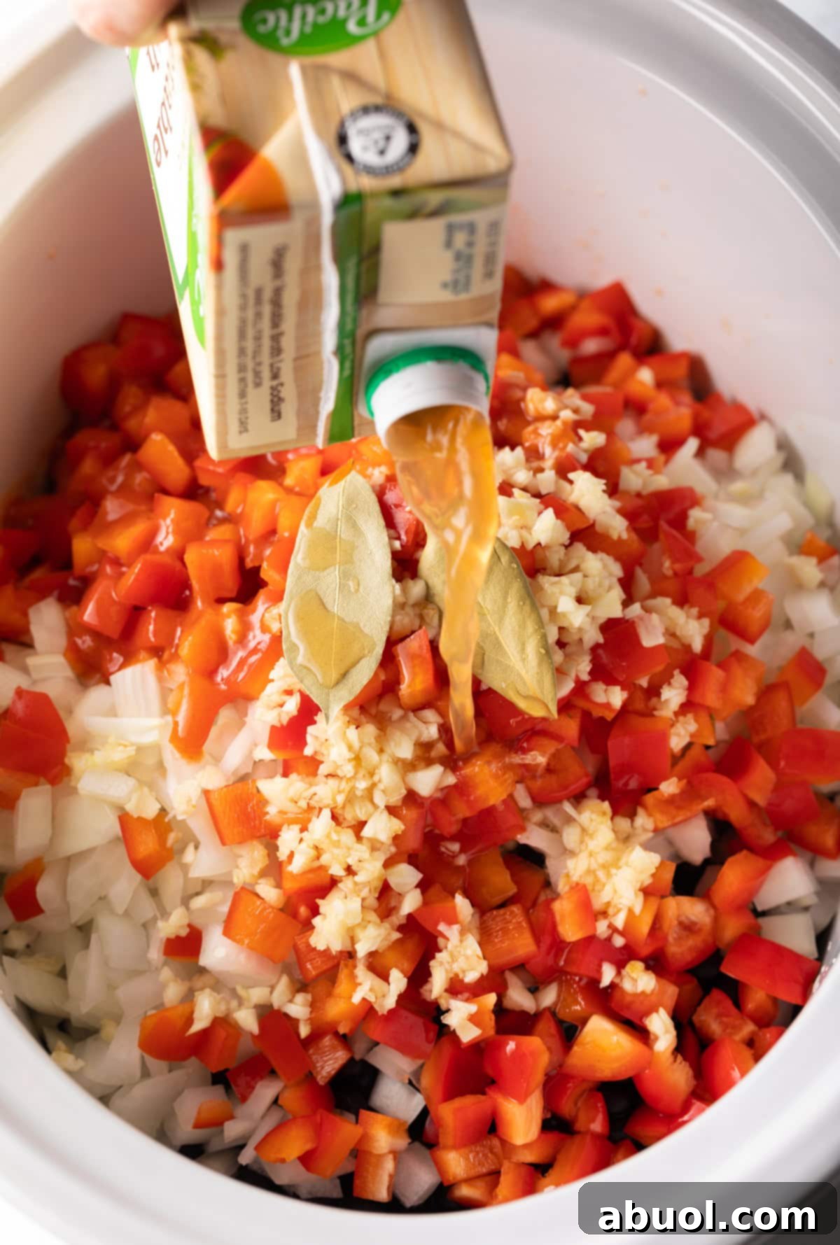 vegetable broth being poured into the slow cooker with black bean soup ingredients