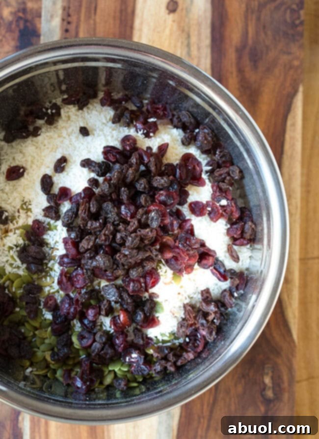 Dried fruit added to nuts and oat mixture in a mixing bowl, for natural sweetness and chewiness.
