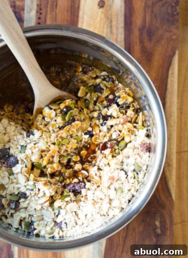 Granola mixture with honey in a mixing bowl with a wooden spoon, showing the binding process.