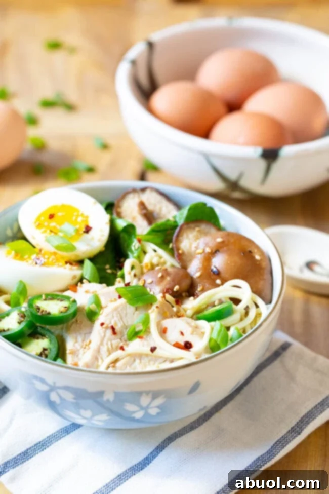 A steaming bowl of Slow Cooker Chicken Ramen Noodle Soup, garnished with a soft-boiled egg, fresh scallions, and sliced chicken.