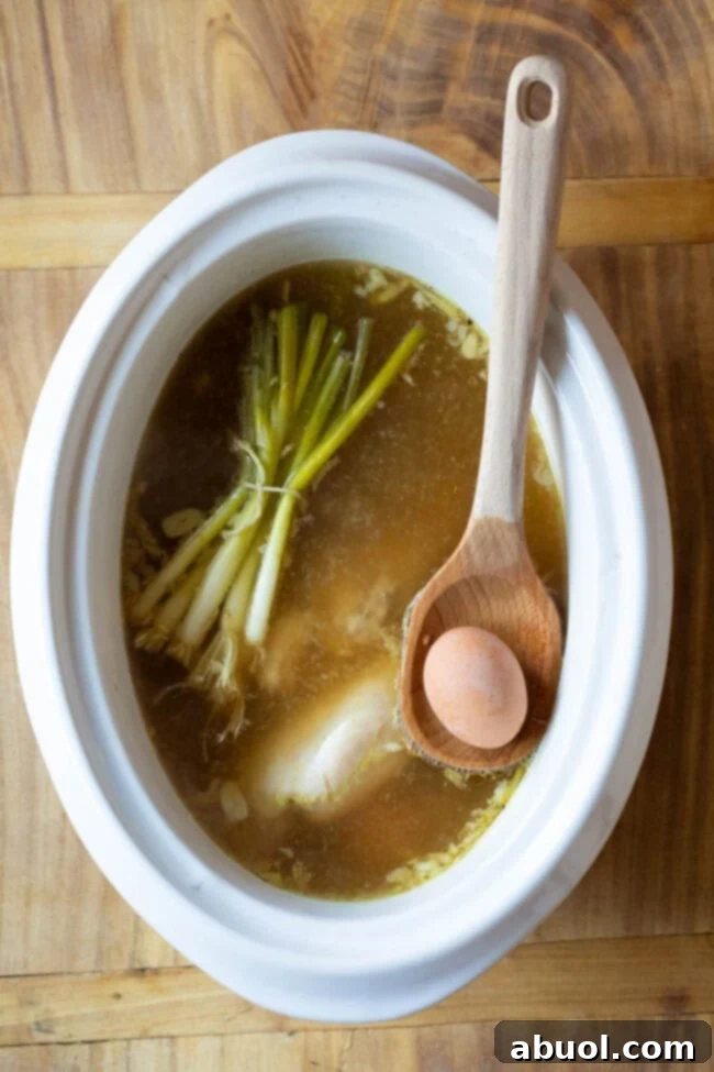 Ingredients for slow cooker ramen, including chicken, eggs, ginger, garlic, and scallions, simmering in dashi broth inside a crockpot.
