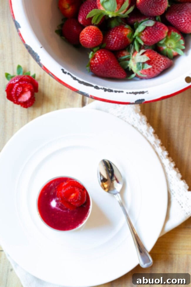 Top down view of a small glass dish showcasing silky Swedish Kreme with a vibrant berry compote and an artful strawberry rose.