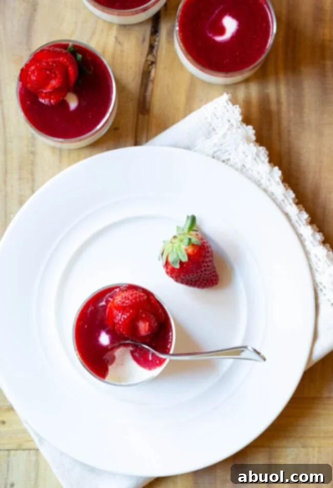 Top down view of a glass dish with silky Swedish cream topped with berry compote and a perfect strawberry rose. A whole strawberry rests beside the dish, ready to be transformed.