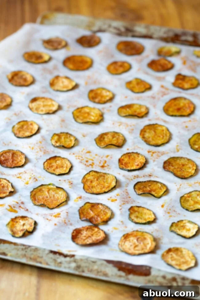 Oven-baked zucchini chips spread on a baking sheet lined with parchment paper, fresh out of the oven.