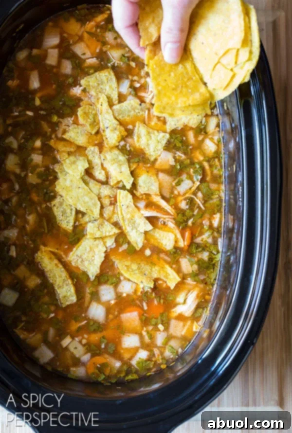 Hand adding crushed corn tortilla chips to the slow cooker of chicken soup.