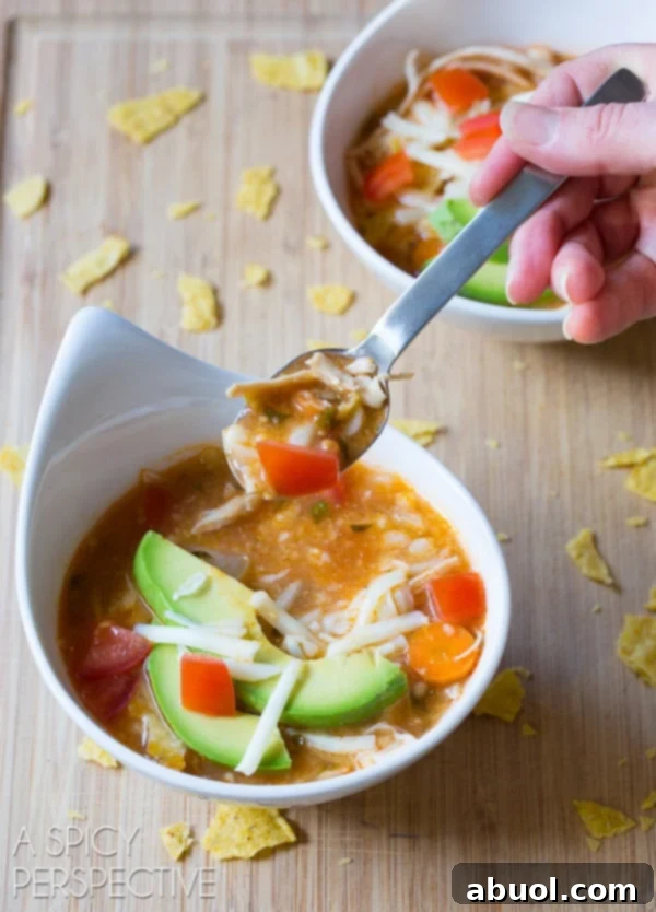 Hand with a spoon scooping a bite of soup from a white bowl.