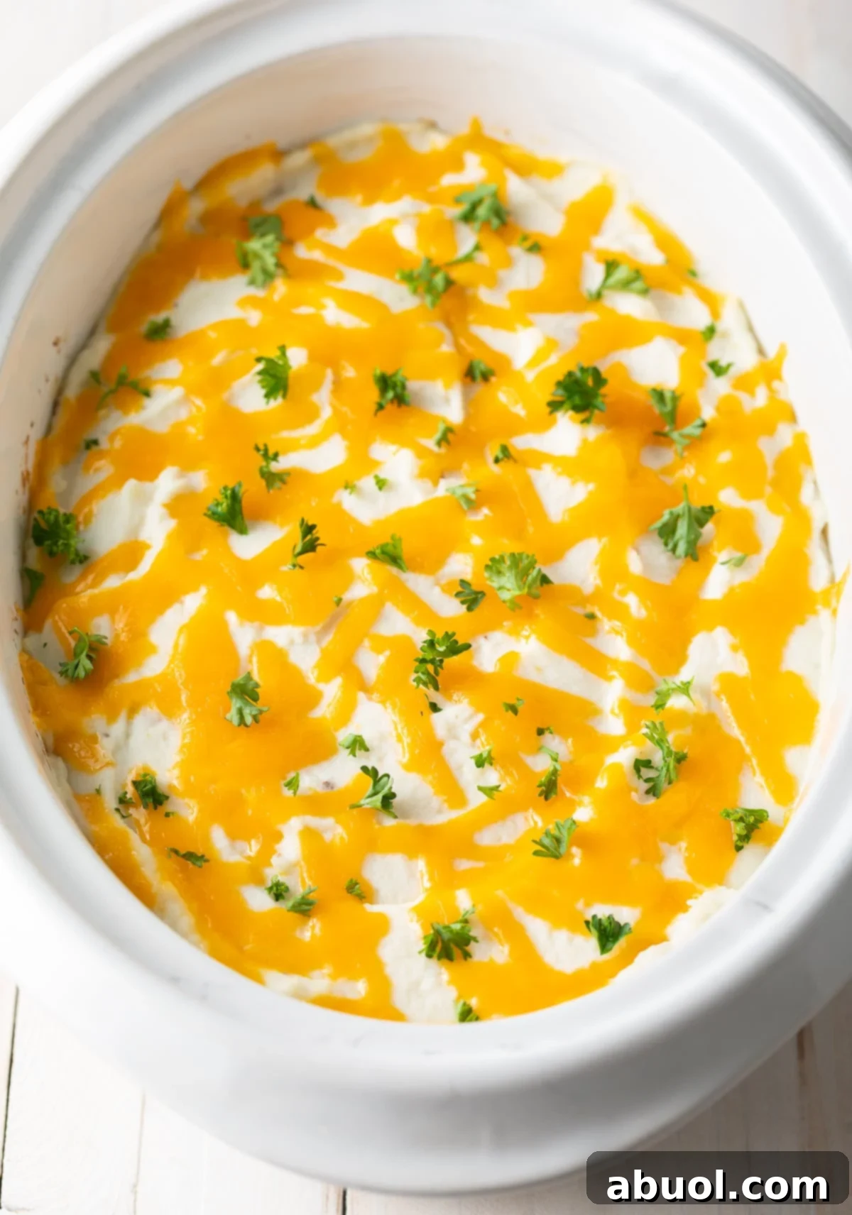 Overhead view of slow cooker Shepherd's pie, golden brown with melted cheese and a sprinkle of fresh parsley.