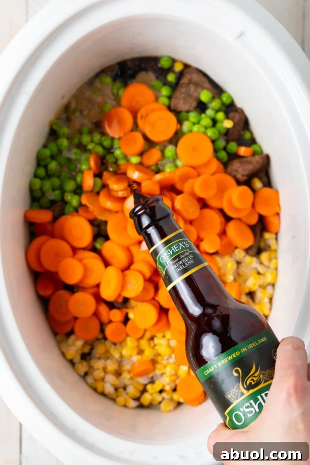 Pouring rich, dark Guinness stout beer over a mixture of meat and vegetables in a slow cooker.