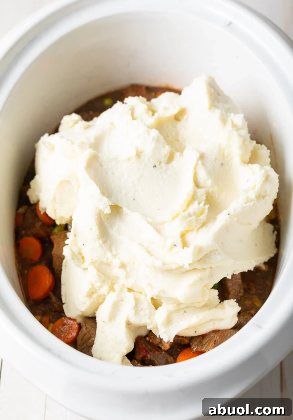 A generous layer of creamy mashed potatoes spread over the rich meat and vegetable mixture in a crockpot.