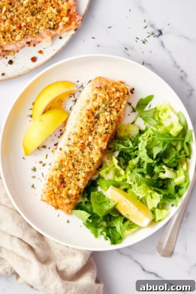 Oven baked salmon with a golden parmesan herb crust, served on a baking sheet with a kitchen spatula beside it.