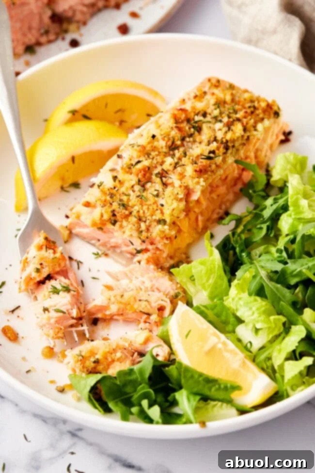 Close-up of baked salmon with a flaky texture visible under the parmesan herb crust.