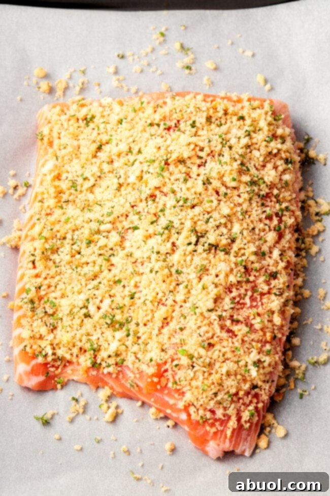 Raw salmon fillet generously covered with the parmesan herb crust on parchment paper, prior to baking.