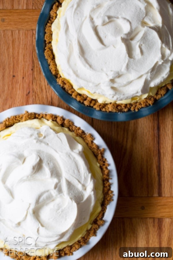 Two lemon cream pies before getting a sprinkle of graham crackers on top of the cream, showcasing the smooth whipped topping.