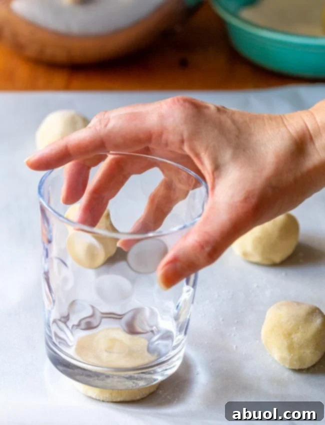 Hands pressing down sugar cookie dough balls with a glass for uniform shape.
