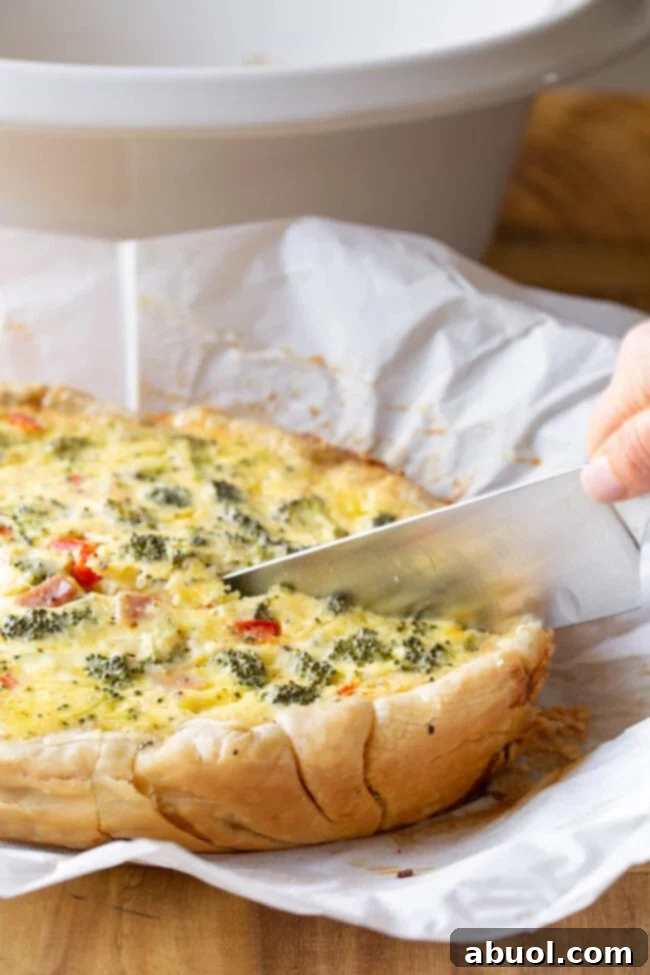 A sharp knife cutting breakfast quiche that's on a piece of parchment paper.