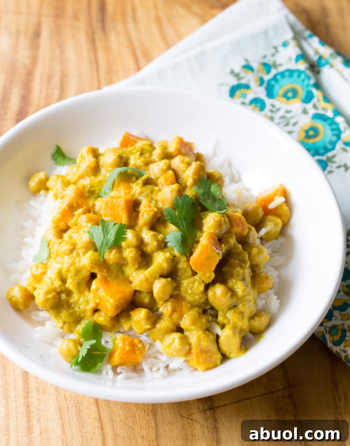 A white plate with a generous serving of creamy crockpot chickpea curry on a bed of fluffy white rice, garnished with fresh cilantro.