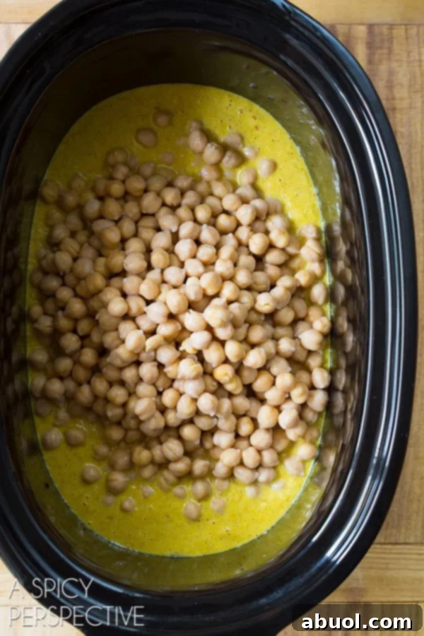 Crockpot filled with a creamy, golden curry sauce and chickpeas, ready for the slow cooking process.