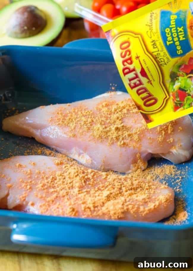 Raw chicken breast in a platter being seasoned with Old El Paso Taco Seasoning.