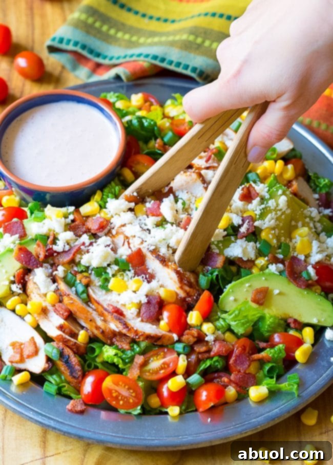 Hand is tossing the Mexican chicken salad in a bowl with wooden tongs.