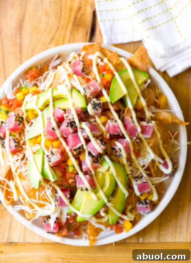 Ahi tuna nachos overhead view, white bowl loaded with crispy wonton chips, cubes of seared ahi tuna, mango pico de gallo, shredded cabbage, avocado slices, and a drizzle of wasabi mayo.
