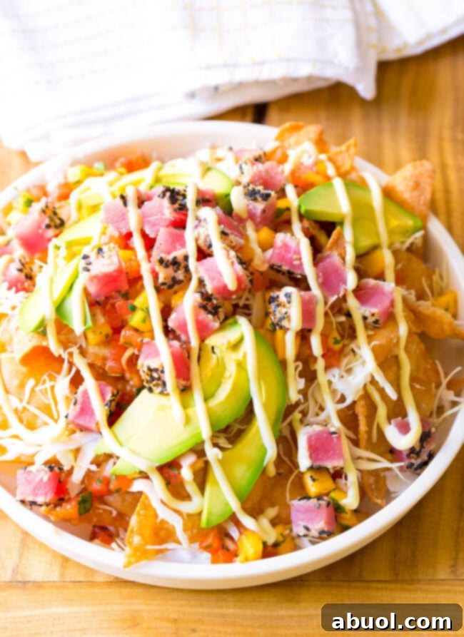 White bowl loaded with crispy wonton chips, cubes of seared ahi tuna, mango pico de gallo, shredded cabbage, avocado slices, and a drizzle of wasabi mayo.