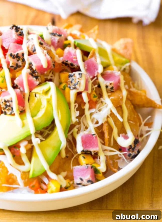 White bowl loaded with crispy wonton chips, cubes of seared ahi poke, mango pico de gallo, shredded cabbage, avocado slices, and a drizzle of wasabi mayo.