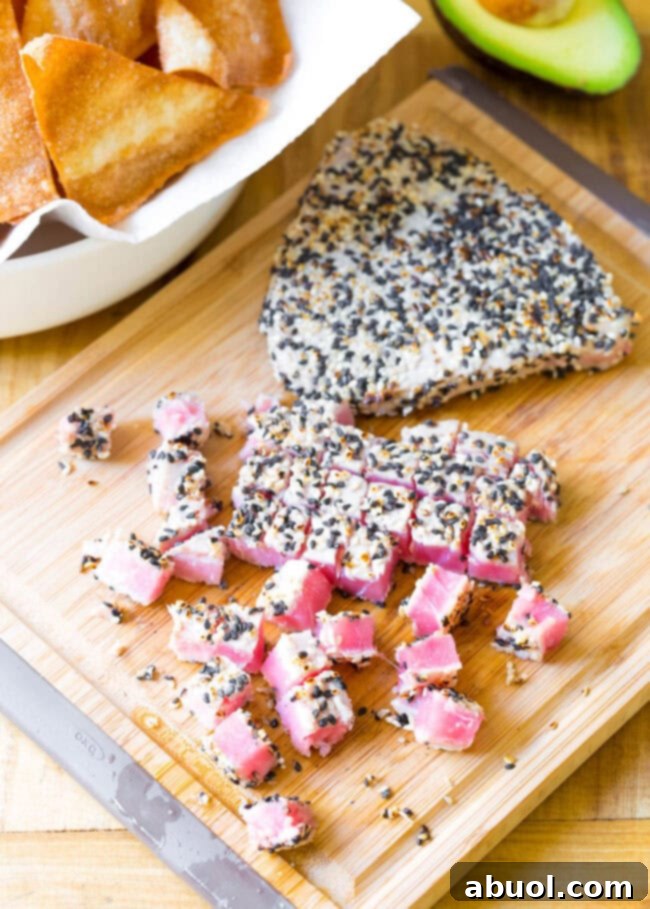 Two seared tuna steaks on a cutting board, one cut into cubes.