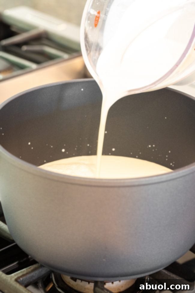 Crafting Creamy Ricotta from Scratch 5 Pouring milk from a glass measuring glass to a large metal pot.
