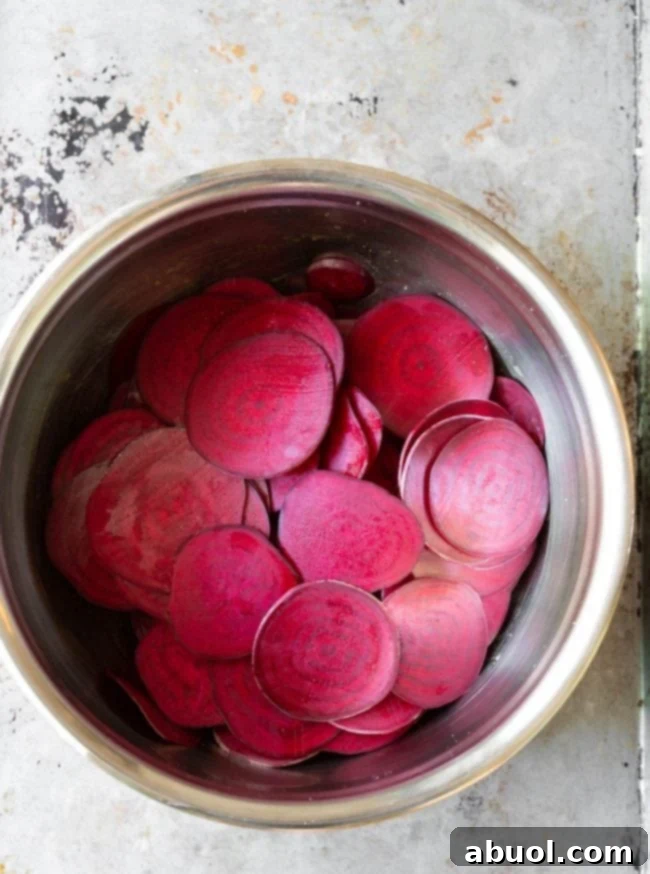 Thinly sliced beetroot pieces coated in olive oil and salt, visibly releasing moisture in a metal bowl during the critical 'sweating' process.