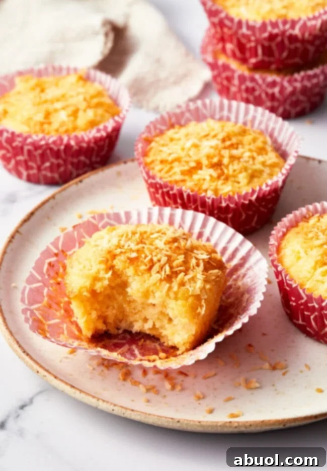 A tropical breakfast muffin with a bite taken out of it on a white plate. more muffins are in the background.