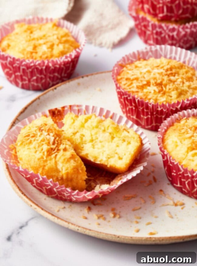 A tropical breakfast muffin split in two on a white plate. More muffins are in the background.