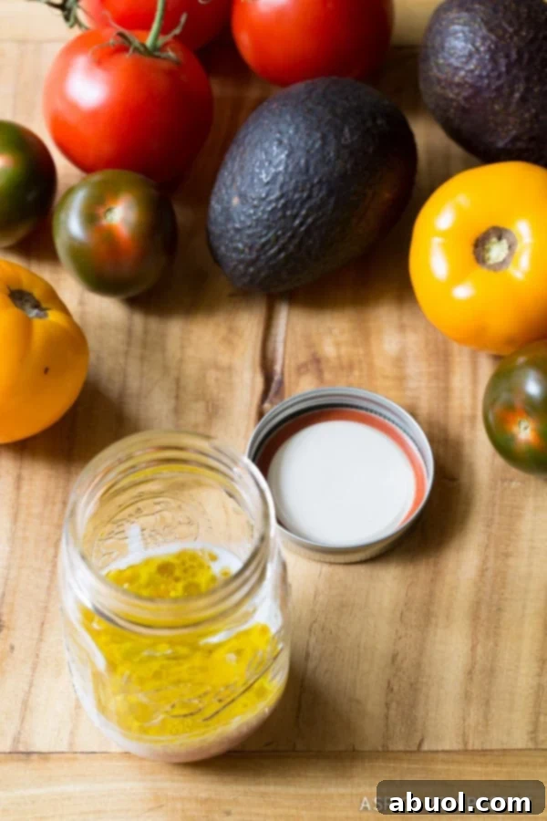 A rustic wood cutting board featuring vibrant red tomatoes and ripe avocados, with a mason jar filled with oil in the background, ready for salad preparation.