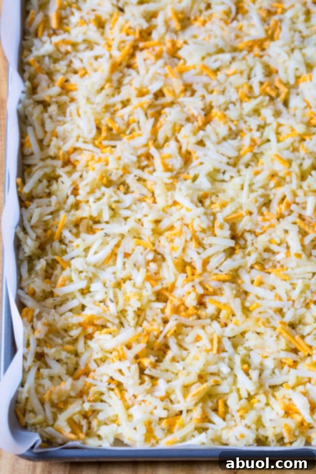 Easy hash browns spread thinly on a baking sheet, ready to be placed in the oven for baking.
