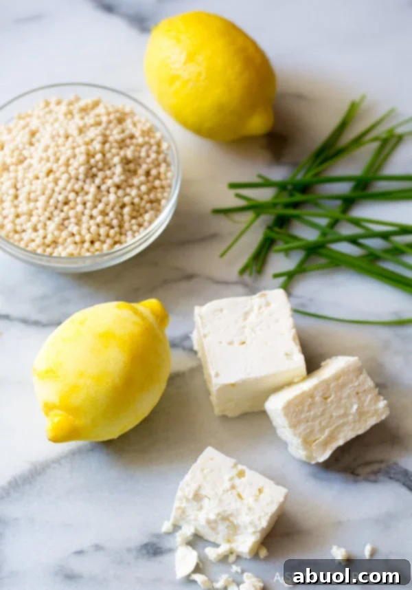 Fresh ingredients for Greek lemon chicken soup neatly arranged on a marble kitchen counter, including lemons, herbs, chicken, and broth.
