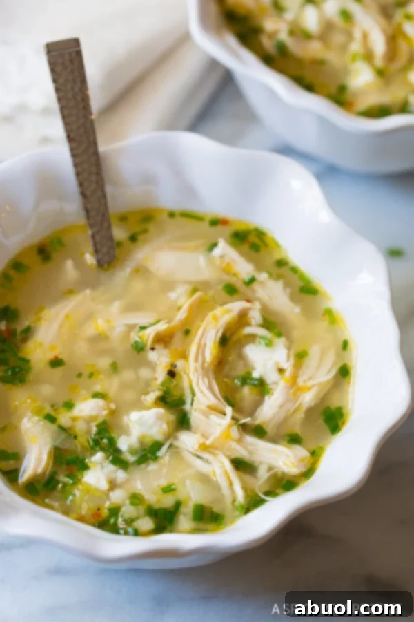 A single white bowl of Greek Lemon Chicken Soup, with a spoon resting in it, showcasing the rich broth and tender ingredients.