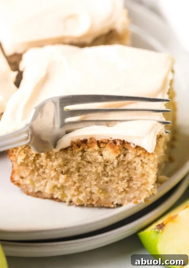 Slice of apple cake with frosting on top with a fork cutting into cake to get a bite.