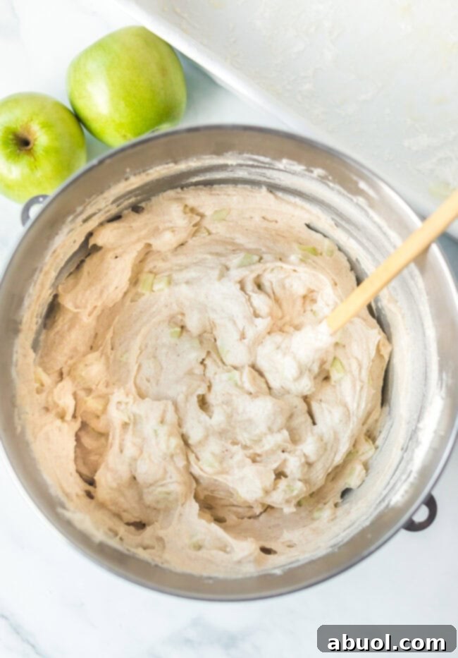 mixing apple into cake batter in a large mixing bowl. 