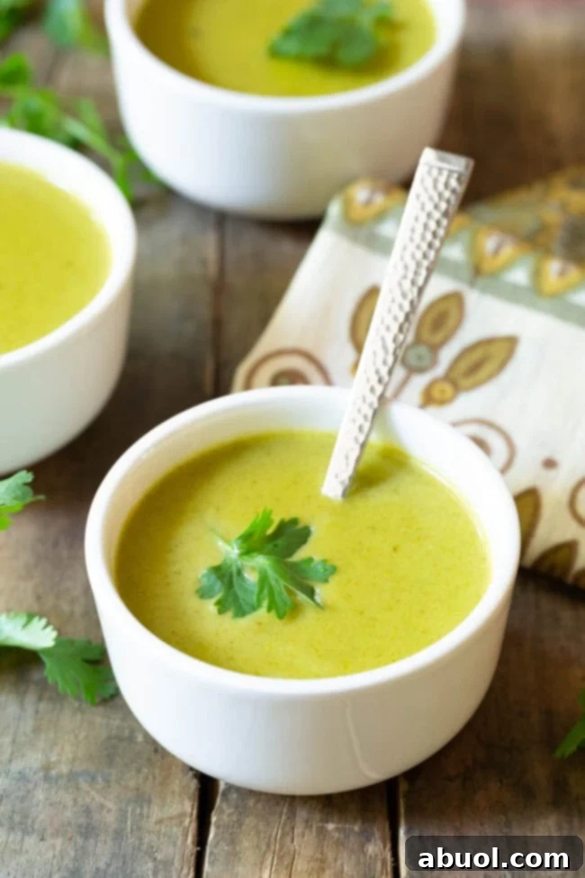 A small white bowl of creamy poblano pepper soup, garnished with a fresh cilantro leaf.