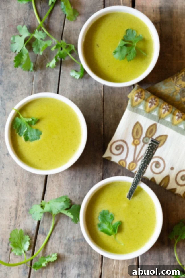 Three small white bowls of creamy green soup, each elegantly garnished with a fresh cilantro leaf, viewed from above.
