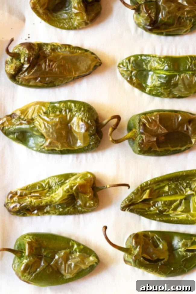 Roasted Poblano Peppers resting on a baking sheet lined with parchment paper, their skins visibly blistered and charred, ready for peeling.