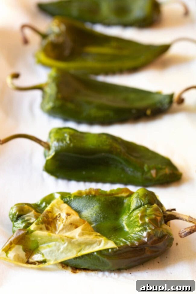 A hand gently peeling the blistered skin off a roasted poblano pepper, showcasing the tender flesh beneath.