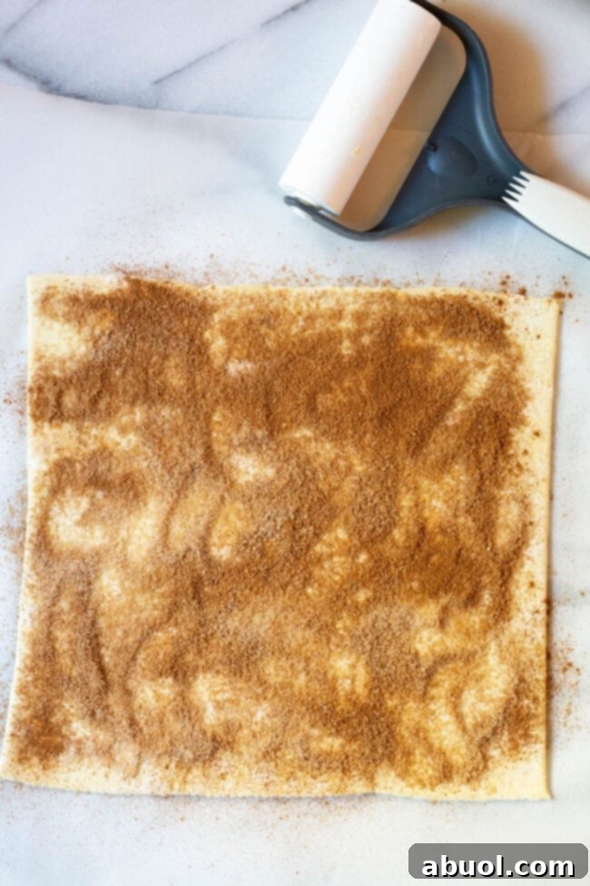 One sheet of puff pastry sprinkled with a cinnamon sugar mixture, ready to be covered with a second sheet.