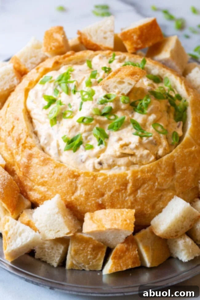 A bread bowl filled with sausage cheese dip on a plate with bread pieces for dipping.