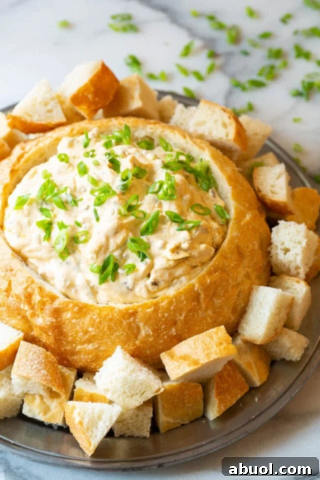 A bread bowl filled with sausage cheese dip on a plate with bread pieces for dipping.