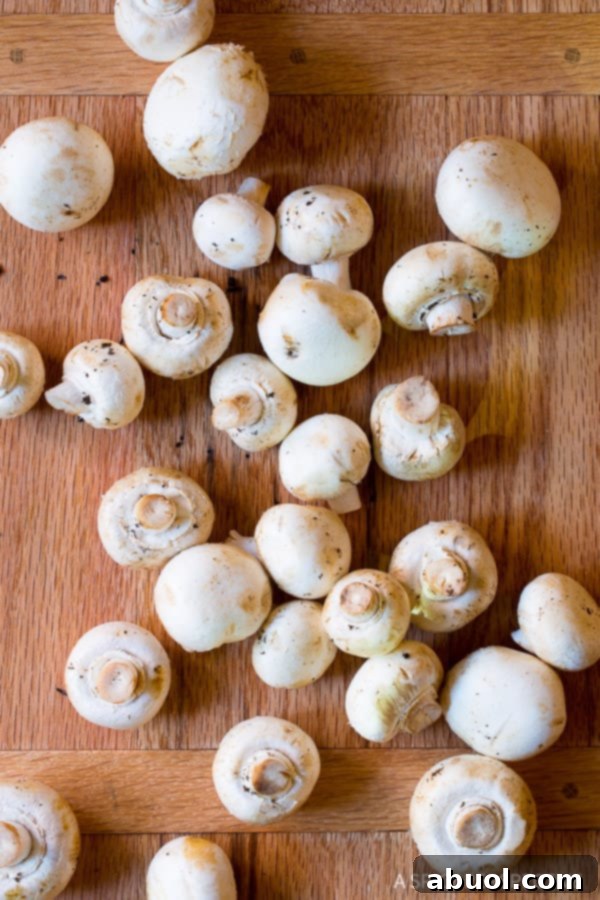 A cutting board piled high with fresh white button mushrooms, ready for cleaning and preparation before being sautéed.