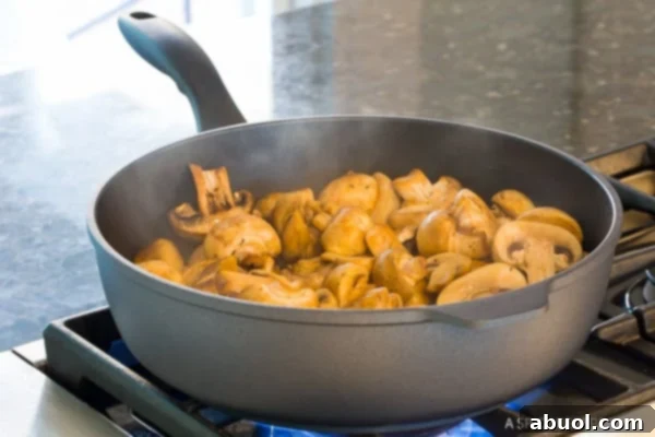 White button mushrooms actively sautéing in a hot pan with butter and olive oil, beginning to brown and release their moisture.